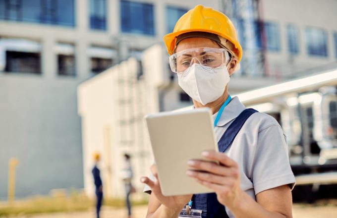 Female construction worker using digital tablet while wearing protective face mask during coronavirus epidemic.